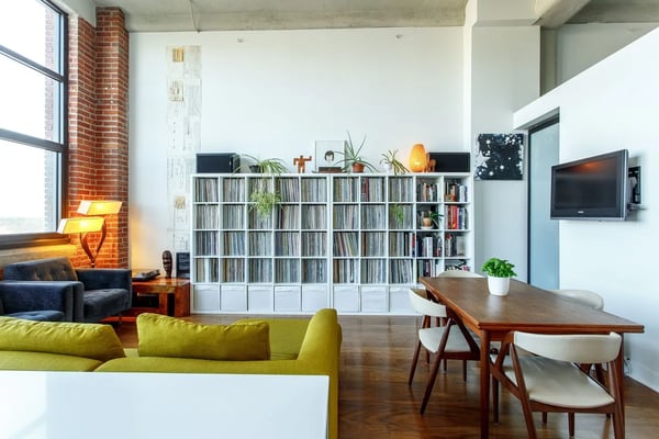 Industrial loft living room with exposed brick, lime-green sofa, media shelving, dining table, and wall-mounted TV